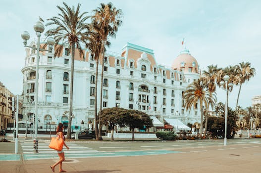 Woman walking by Hotel Negresco with palm trees in Nice, France during summer.